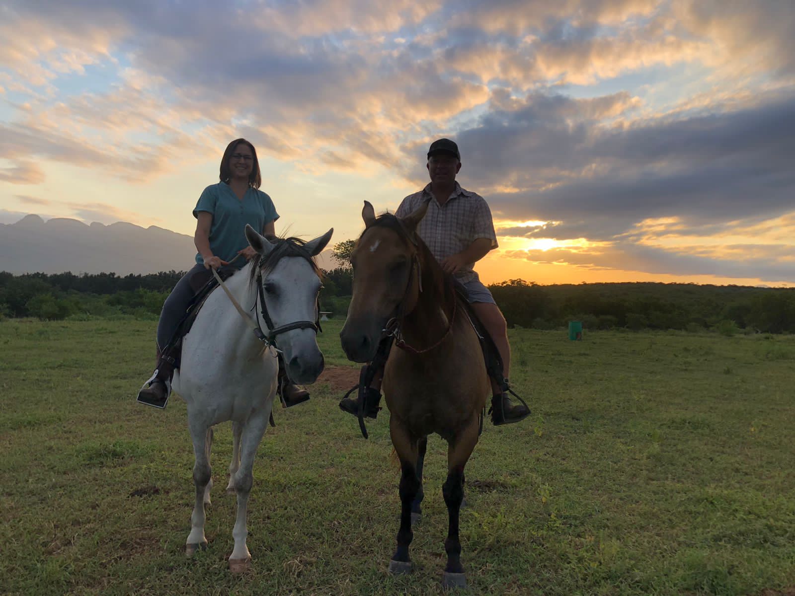 Two riders on white and chestnut horses at sunset